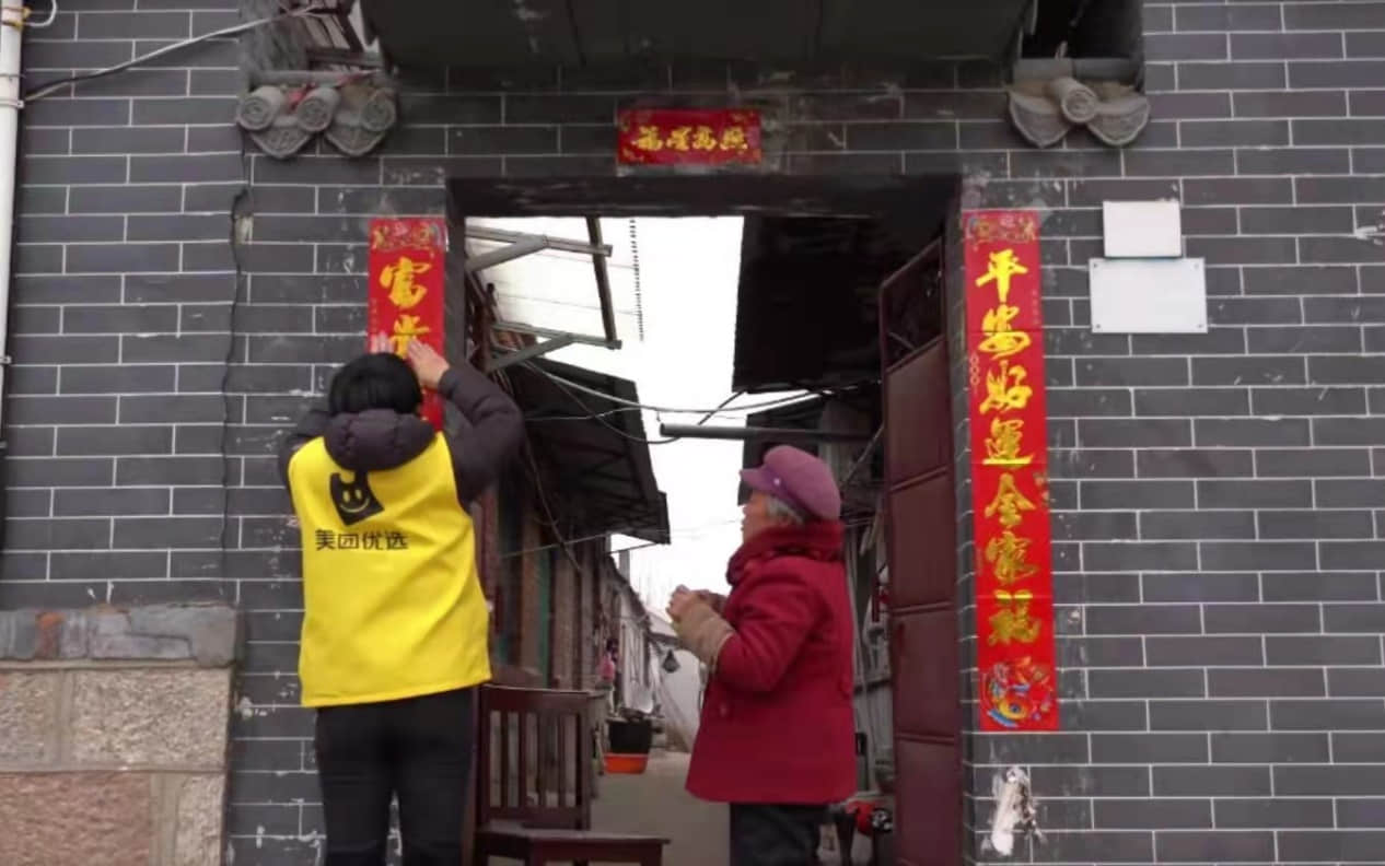 ▲美團(tuán)優(yōu)選店長孫維丹幫馬奶奶把春聯(lián)貼好，小島需要年輕人 （攝影：胡慧）
